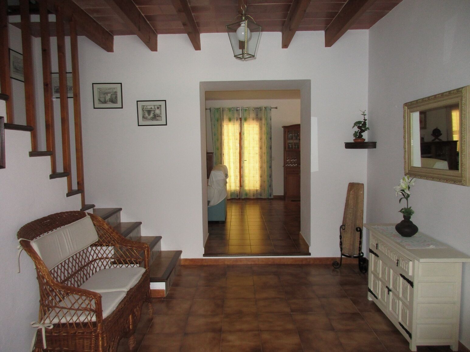 A spacious living area with a wooden staircase, a wicker sofa, a white cabinet, and a mirror on the wall.