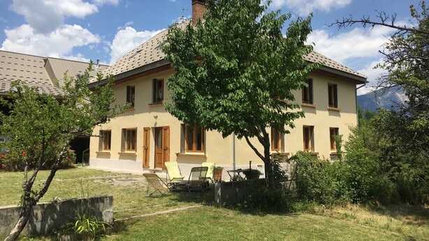Ein zweistöckiges Haus mit einem Ziegeldach, ein großer Baum im Vorgarten und ein klarer Himmel.