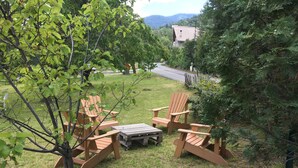 Eine grüne Sitzgelegenheit im Freien mit Holz-Adirondack-Stühlen und einem kleinen Tisch, umgeben von Bäumen und einem Gebäude im Hintergrund.