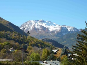 A mountain with snow-capped peaks, surrounded by forested hills and a few buildings. - Large apartment in mountain house in Risoul - 05600 (Risoul)