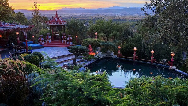 Um jardim tranquilo com lago, gazebo e vista para montanhas ao longe.