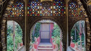 Um corredor ornamentado com vitrais elaborados e uma escadaria central que leva a uma porta.