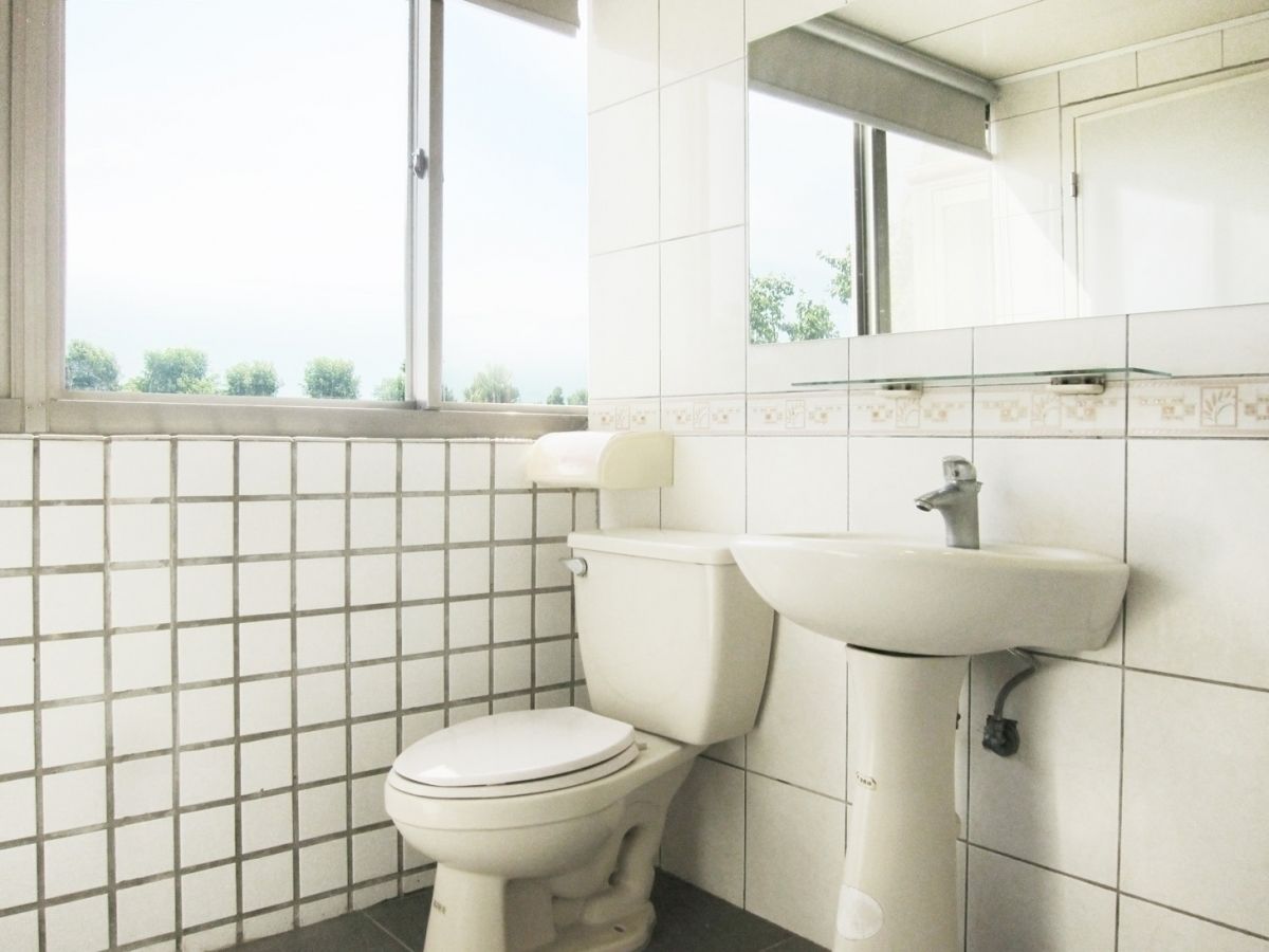 Un baño con inodoro, lavabo y paredes de azulejos, además de un ventanal.