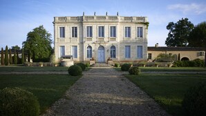 Un grand bâtiment symétrique, doté d’une entrée centrale, entouré de jardins bien entretenus et d’un chemin de gravier menant à la porte.