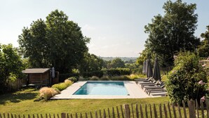 Une piscine rectangulaire dotée d’une terrasse en bois, entourée d’une végétation luxuriante et d’une clôture en bois.