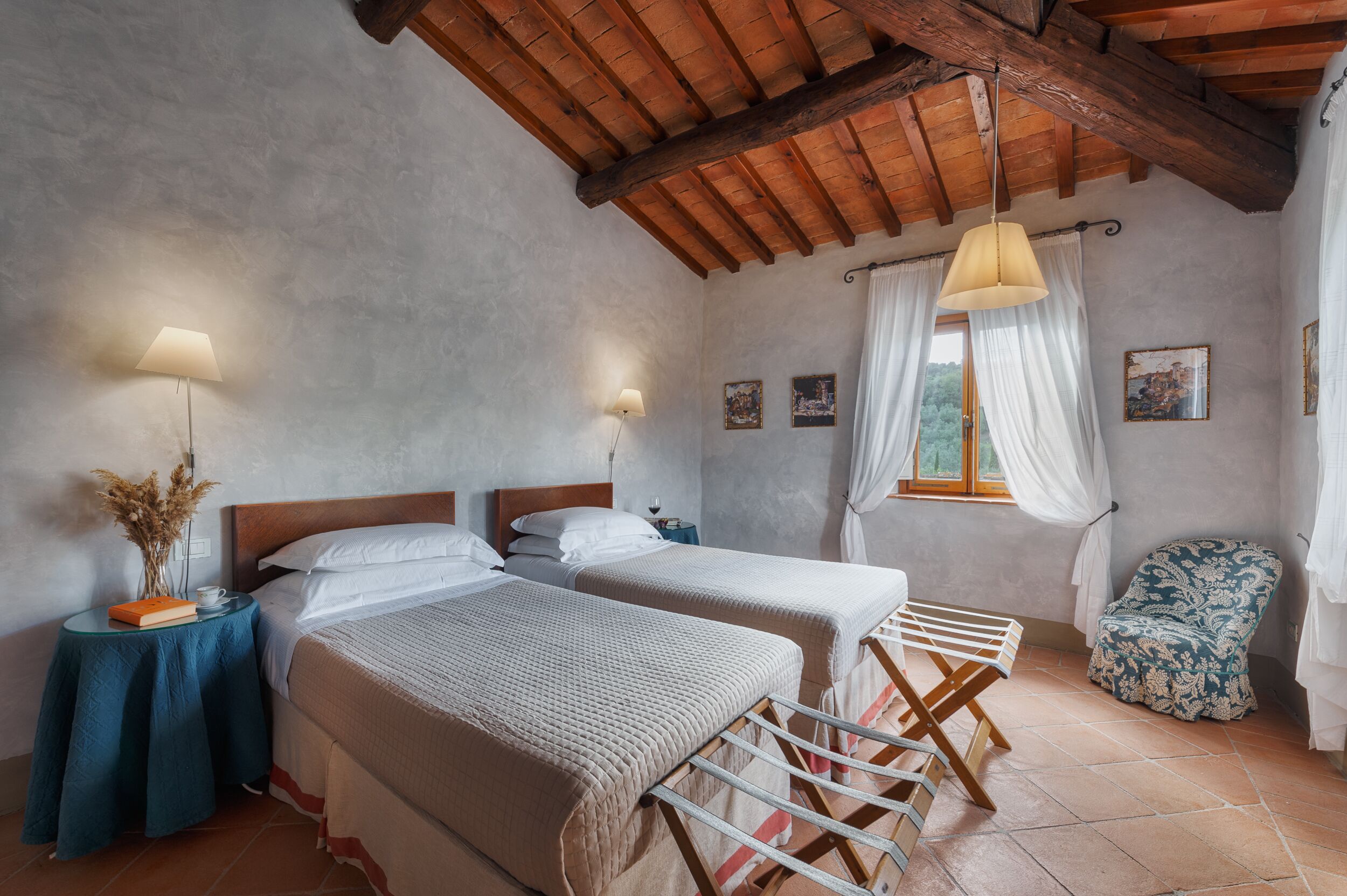A bedroom with two beds, a wooden ceiling, a window with curtains, and a chair.