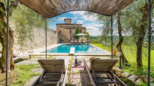 A pool area with lounge chairs, a table with a bottle, and a view of a stone building. - Villa just 14 km to Florence, 8 bedrooms. Garden, private pool and Wi-Fi! (Rignano sull'Arno)