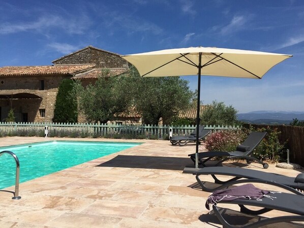 A swimming pool with lounge chairs and an umbrella, surrounded by stone buildings and greenery.