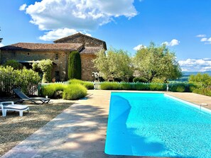 A stone building with a tiled roof, a swimming pool, and a well-maintained garden with a white picket fence.