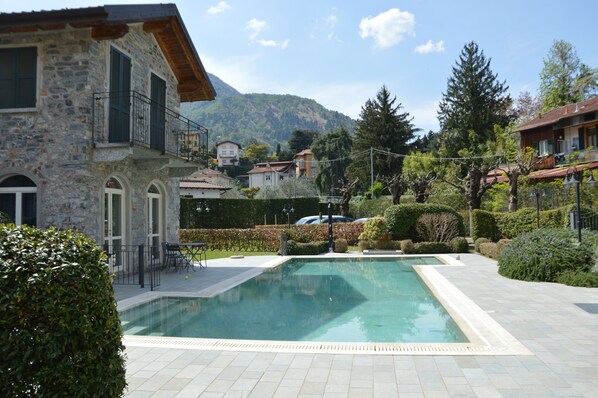 A stone building with a pool, surrounded by greenery and mountains.