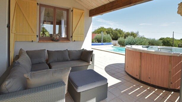 A covered outdoor seating area with a sofa and ottoman, a hot tub, and a view of a swimming pool and greenery. - Villa Retreat with Pool and pets (Vélieux)
