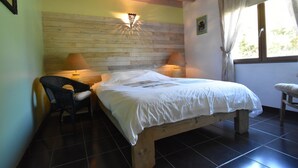 A bedroom with a wooden headboard, two bedside lamps, a bed with white linens, a chair, and a window with curtains. - Villa Retreat with Pool and pets (Vélieux)