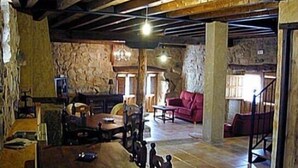A rustic interior with exposed wooden beams, stone walls, a red sofa, and a stone fireplace.