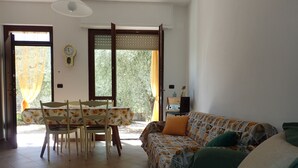 Una sala de estar con un sofá, una mesa de comedor con sillas y un ventanal con cortinas.