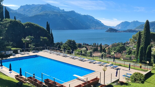 A swimming pool with lounge chairs, a fenced area, and a view of mountains and a lake. - Italian Lake Apartment With Large Swimming Pool, Tennis Court, Lake Views, WiFi (Menaggio)