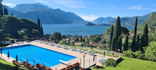 Une piscine avec des chaises longues, un espace délimité par une clÎture et une vue sur les montagnes et un lac.