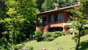 A two-story house with a balcony, surrounded by lush greenery and trees. - Italian Lake Apartment With Large Swimming Pool, Tennis Court, Lake Views, WiFi (Menaggio)