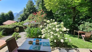 A garden with a table set for dining, surrounded by lush greenery and flowering plants. - Italian Lake Apartment With Large Swimming Pool, Tennis Court, Lake Views, WiFi (Menaggio)
