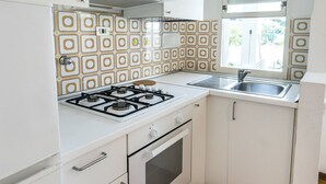 Eine Küche mit weißen Schränken, einem Gasherd, einem Backofen, einer Spüle und einer Fliesenrückwand mit Muster.