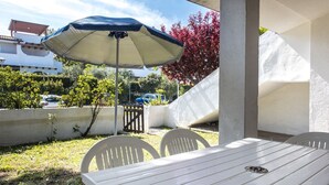 Eine Terrassengruppe im Freien mit Tisch, Stühlen und einem blau-weißen Sonnenschirm an einer weißen Wand.