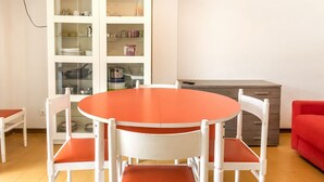 Ein Essbereich mit einem runden Tisch, vier Stühlen, einer weißen Schrank mit Glastüren und einem roten Sofa.