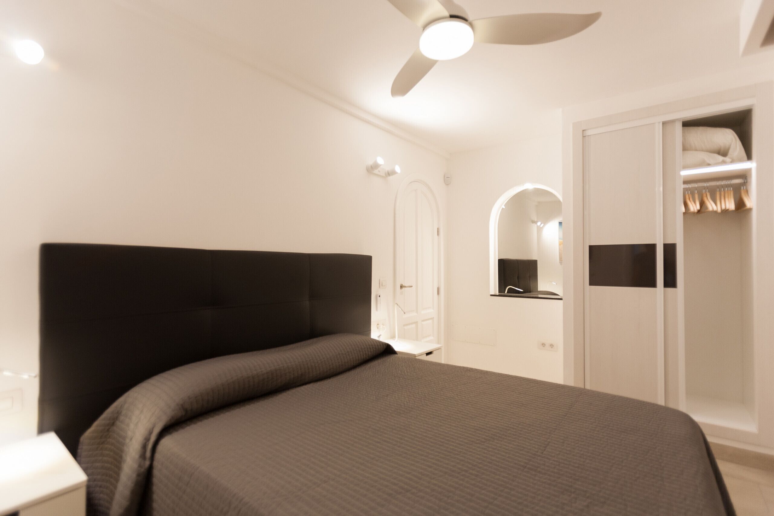 A bedroom with a bed, a wardrobe, a mirror, and a ceiling fan.
