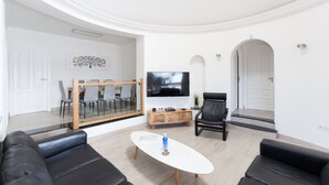 A modern living room with a flat-screen TV, a coffee table, and black leather sofas.