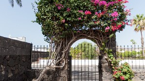 A stone archway with pink flowers, leading to a gated entrance.
