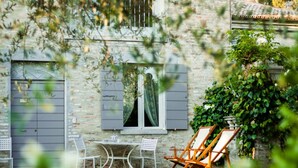 A rustic stone building with a window, shutters, and a table with chairs outside. - On the ground floor of an old farmhouse, in the countryside with a swimming pool (Pesaro)