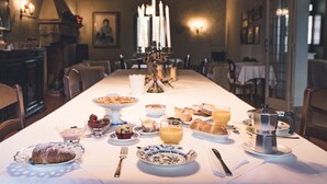 A dining table set with various breakfast items, including pastries, fruit, and beverages, in a warmly lit room with a chandelier and framed artwork on the walls. - On the ground floor of an old farmhouse, in the countryside with a swimming pool (Pesaro)