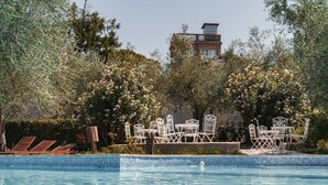 A swimming pool with lounge chairs and a table set up for dining, surrounded by trees and a building in the background. - On the ground floor of an old farmhouse, in the countryside with a swimming pool (Pesaro)