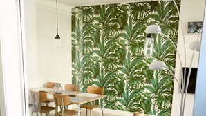 A modern living room with a glass partition, a patterned wall, a dining area with chairs and a table, and a floor lamp.