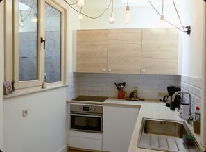 Compact kitchen with light wood cabinetry, stainless steel sink, oven, and ample countertop space.