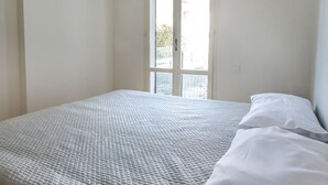 A single bed with a textured white bedspread, a white pillow, and a window with a view of a fence and greenery outside. - M050 - Marcelli, three-room apartment with garden 200 meters from the sea (Marcelli)