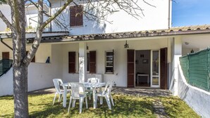 A white building with a covered patio, a table with chairs, and a tree. - M050 - Marcelli, three-room apartment with garden 200 meters from the sea (Marcelli)