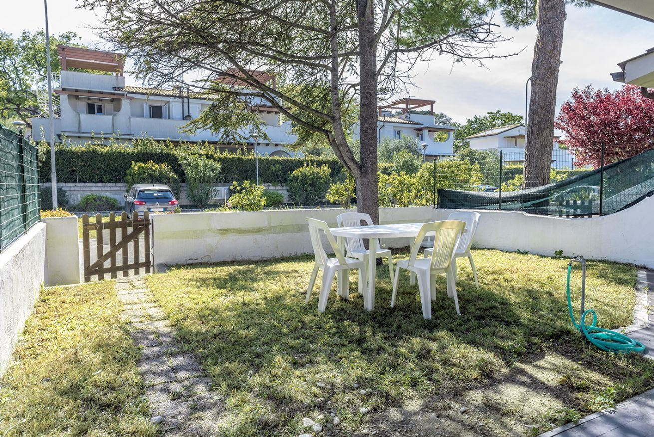A patio with a table and chairs, a tree, and a hose.