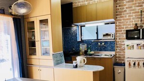 A compact kitchen with a microwave, toaster, and a small refrigerator. There is a wooden cabinet with glass doors and a countertop with a kettle and a cup.