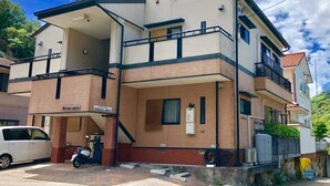 A two-story building with a flat roof, a balcony on the upper floor, and a garage with a scooter parked inside.