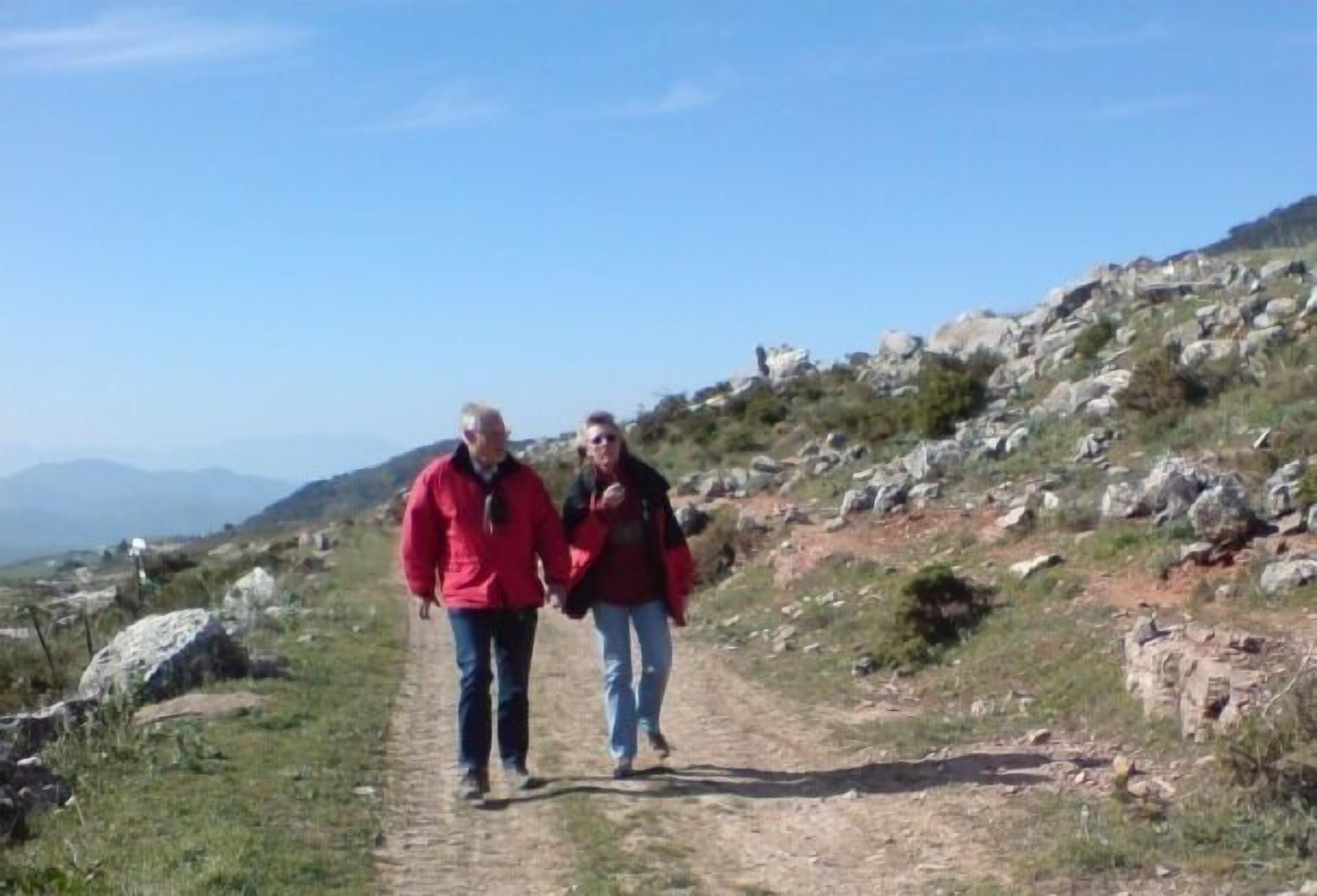 Two people walking on a rocky path surrounded by hills.