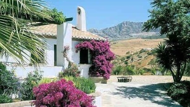 A white building with a tiled roof, surrounded by lush greenery and a mountain in the background. - Holiday home in a traditional finca in the heart of Andalusia (Antequera)