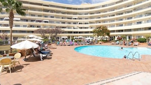 Ett hotell med flera våningar, med en central pool omgiven av solstolar och parasoller.