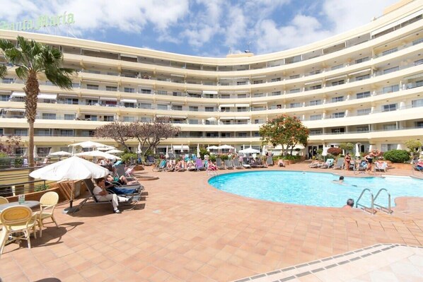 A multi-story hotel with a central swimming pool, outdoor seating, and a palm tree.