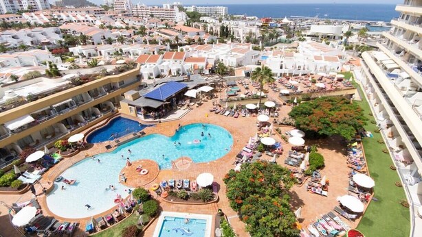 Ett semesterhotell med flera pooler, solstolar och utsikt över havet.
