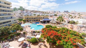 Ett semesterhotell med en stor pool, solstolar och utsikt över den omgivande staden.