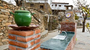 A stone wall with a green pot on top, a brick structure with a sink, and a stone building in the background.