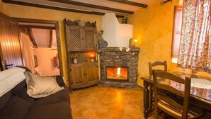 A cozy living room with a stone fireplace, a wooden sofa, and a dining table with chairs.