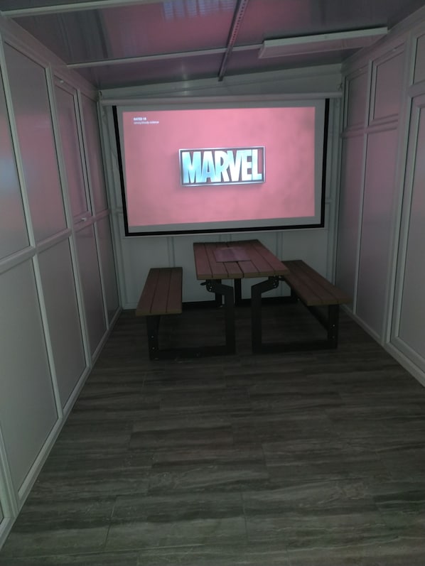 A room with a large screen displaying 'MARVEL', two wooden benches, and a wooden floor. - 5 Luxurious Bed Room House Corporate Let Air Conditioning (London)