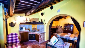 Una cucina compatta con forno a microonde, piano cottura e zoccolo piastrellato. C'è un'area pranzo con tavolo e sedie, e un letto sullo sfondo.