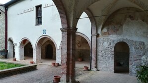 Un cortile con archi in mattoni, un edificio bianco con una finestra e piante in vaso.