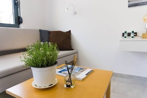 A room with a sofa, a table with a potted plant, a magazine, and a small bottle.
